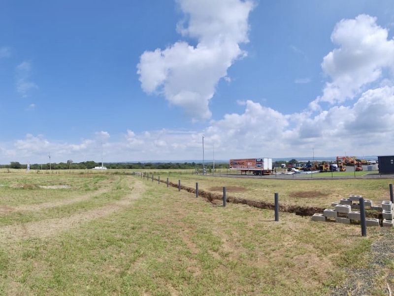Wide-angle view of an expansive industrial plot featuring open land, perimeter fencing, and an unpaved access road.