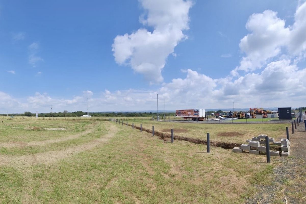 Wide-angle view of an expansive industrial plot featuring open land, perimeter fencing, and an unpaved access road.