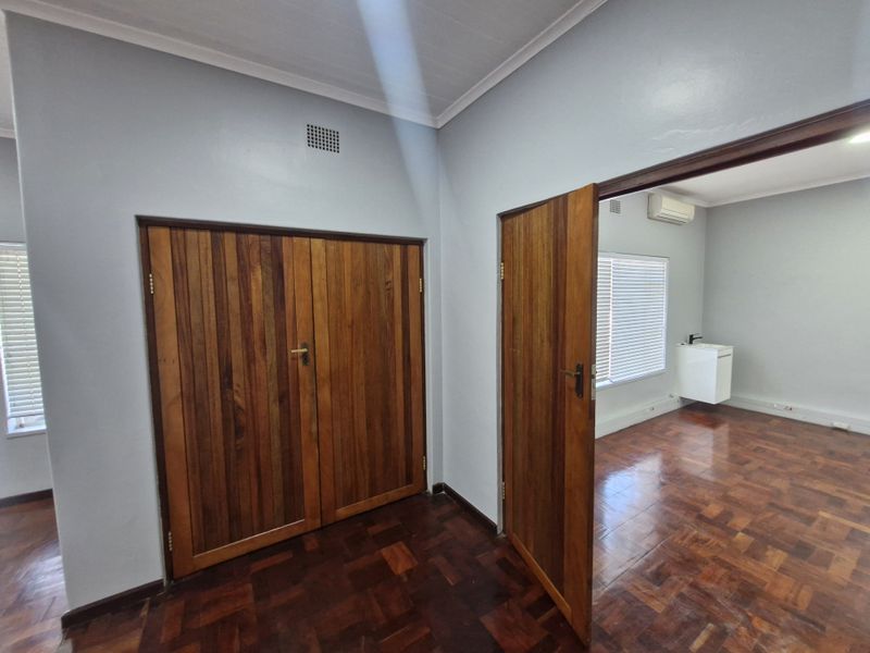 Bright office space featuring polished parquet flooring, wooden doors, built-in storage, and an air conditioning unit, offering a clean and professional work environment.