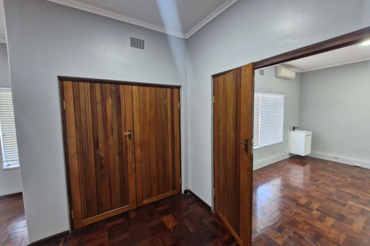 Bright office space featuring polished parquet flooring, wooden doors, built-in storage, and an air conditioning unit, offering a clean and professional work environment.