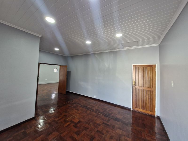 A bright, empty office space featuring polished parquet flooring, a timber panelled ceiling with recessed lighting, and a solid timber door.