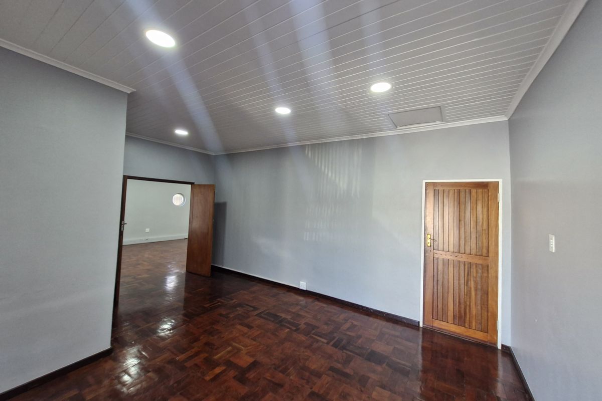 A bright, empty office space featuring polished parquet flooring, a timber panelled ceiling with recessed lighting, and a solid timber door.
