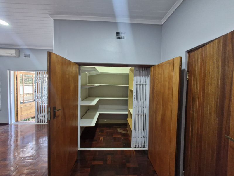 A functional utility or storage space featuring built-in shelving, parquet flooring, and secure timber double doors within an office environment.