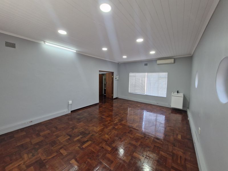 A spacious, empty office area featuring polished parquet flooring, recessed ceiling lighting, a wall-mounted basin, and a split-system air conditioning unit.