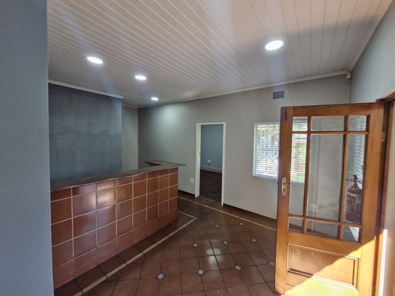 Office reception area featuring a built-in tiled counter, terracotta flooring, recessed lighting, and a timber-framed glass entrance door.