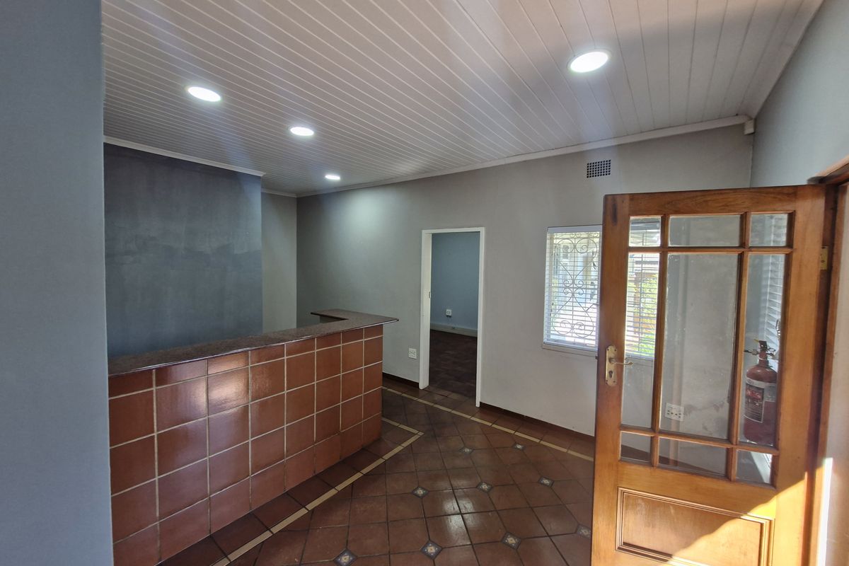 Office reception area featuring a built-in tiled counter, terracotta flooring, recessed lighting, and a timber-framed glass entrance door.