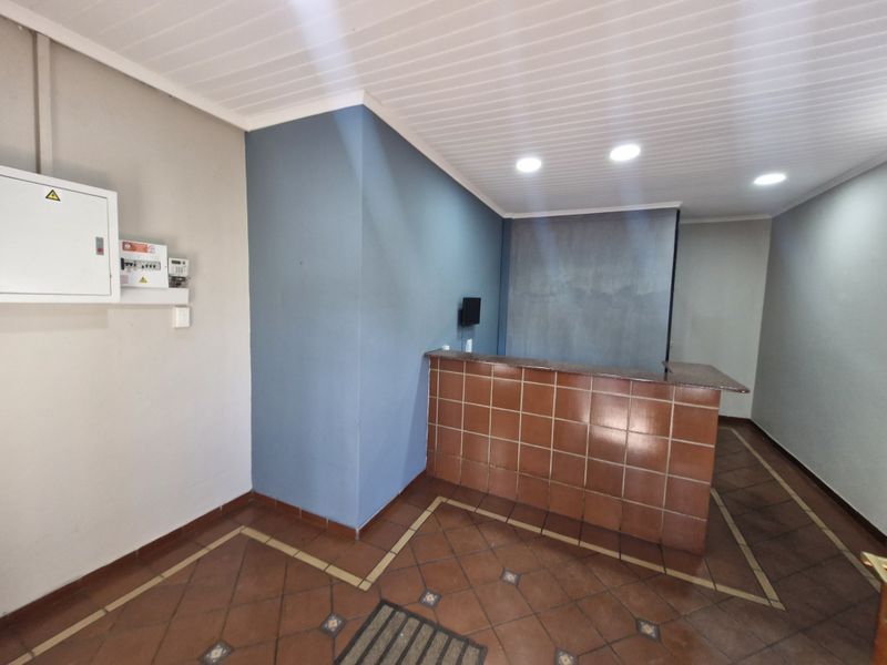 An empty office space featuring a tiled reception counter, recessed downlights, and tiled flooring with a neutral color palette.