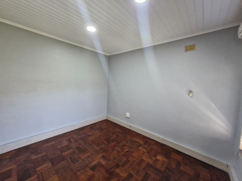 A clean, empty office space featuring polished parquet flooring, recessed ceiling lighting, and a wall-mounted air conditioning unit.