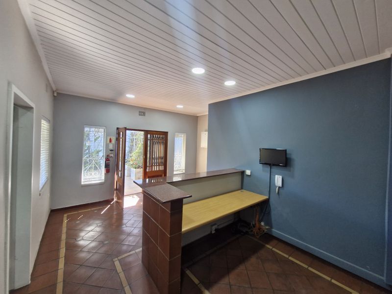 A bright office reception area featuring a built-in desk, tiled flooring, recessed lighting, and direct access to an outdoor area through a security gate.