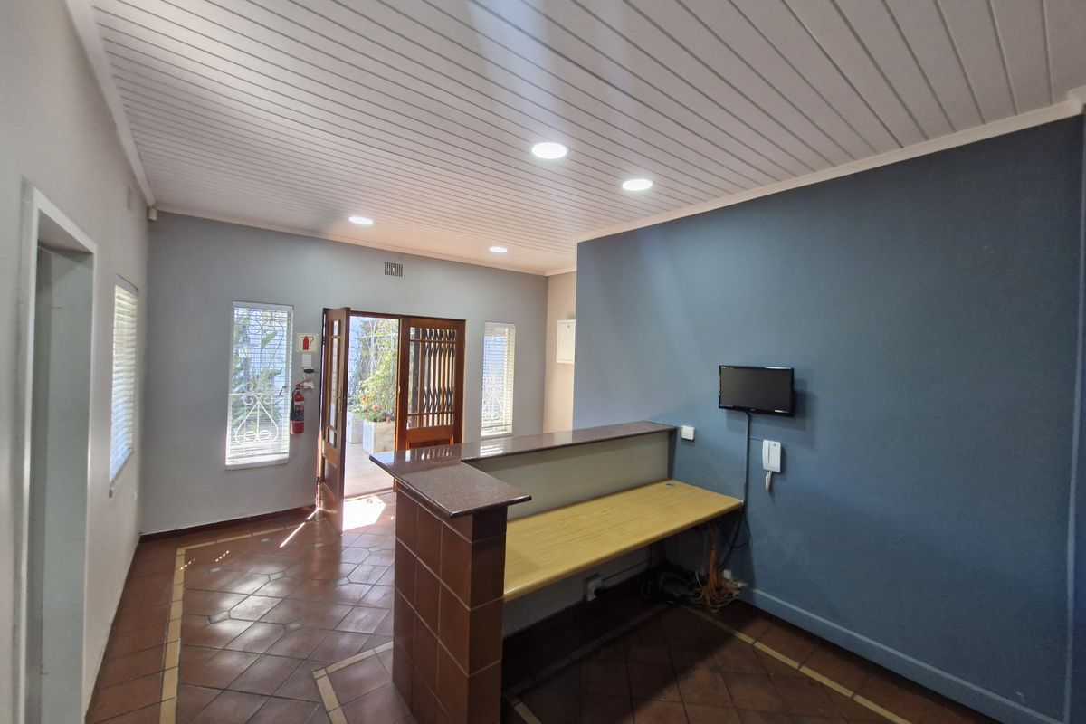 A bright office reception area featuring a built-in desk, tiled flooring, recessed lighting, and direct access to an outdoor area through a security gate.