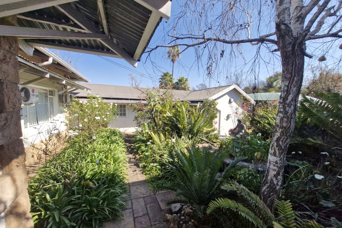 A well-maintained rear garden area featuring a paved walkway, lush established greenery, and views of the office building exterior.