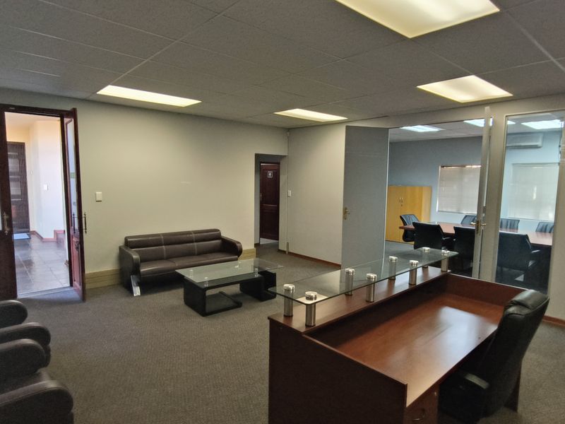 A professional office reception area featuring a built-in reception desk, glass partitions, suspended ceilings, and carpeted flooring with an adjacent meeting room.