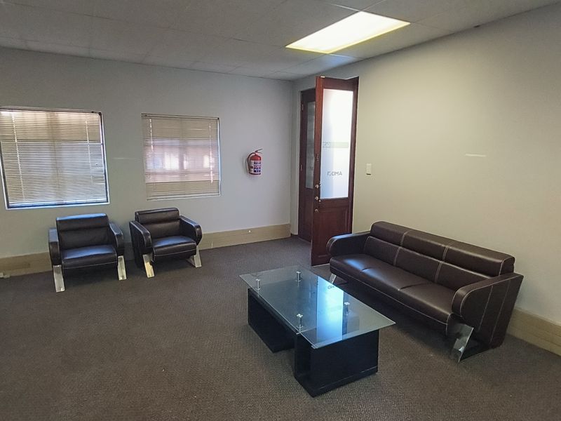 A functional office reception or waiting area featuring carpeted flooring, suspended ceiling with recessed lighting, and wall-mounted air conditioning.