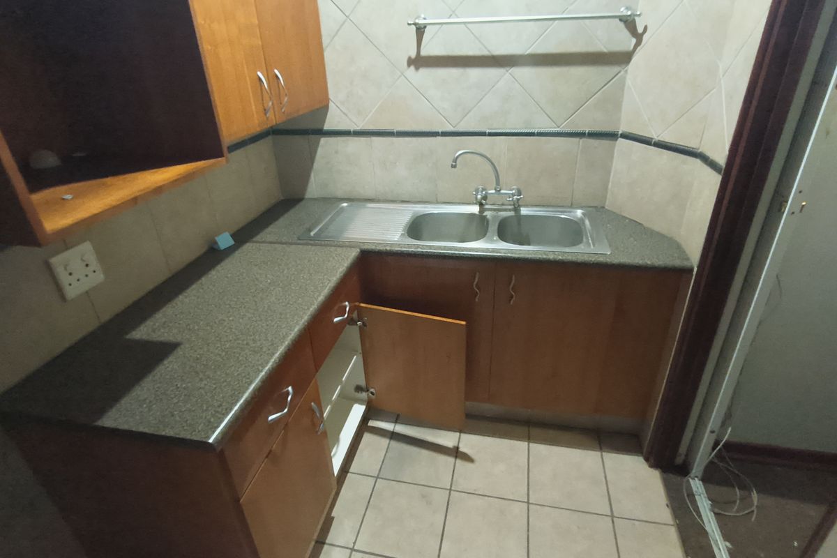 A compact kitchen area featuring built-in wooden cabinetry, a double bowl sink, and tiled finishes, currently requiring minor repairs to cabinet hardware.