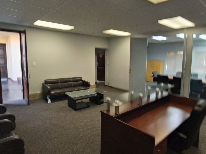 A professional office reception area featuring carpeted flooring, a suspended ceiling with recessed lighting, and a glass partition wall leading to a meeting room.