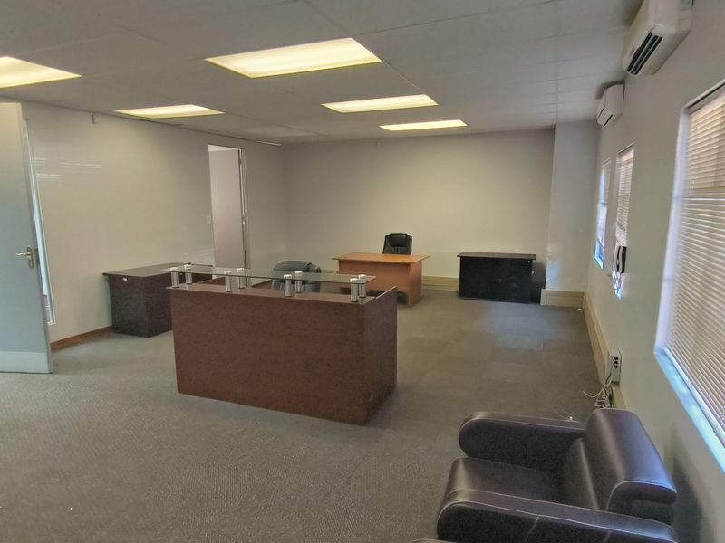 A functional office space featuring a suspended ceiling with recessed lighting, wall-mounted air conditioning units, and carpeted flooring.