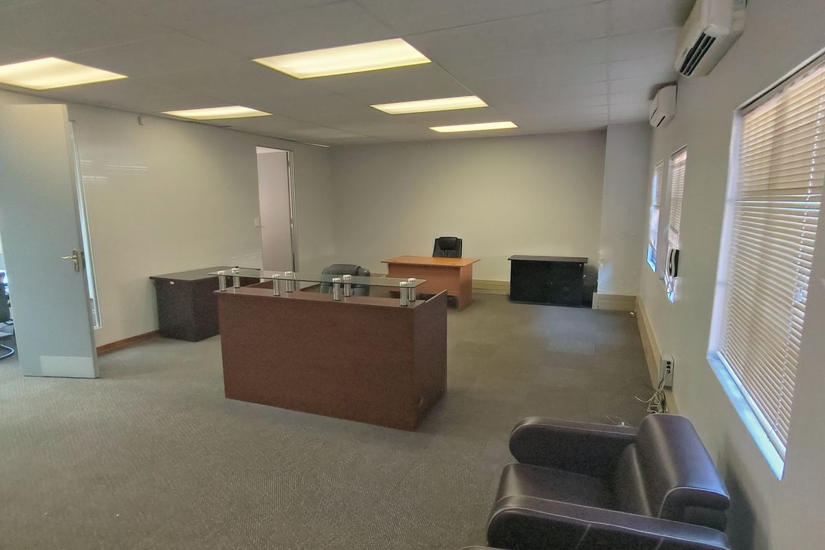 A functional office space featuring a suspended ceiling with recessed lighting, wall-mounted air conditioning units, and carpeted flooring.