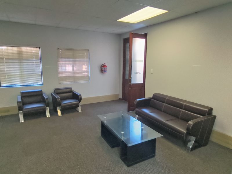 A functional office reception or waiting area featuring a drop ceiling, recessed lighting, wall-mounted air conditioning, and a fire safety unit.