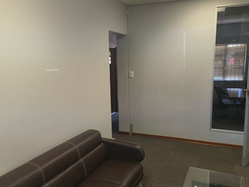 A functional office space featuring carpeted flooring, a glass partition wall, and neutral wall finishes, suitable for a professional work environment.