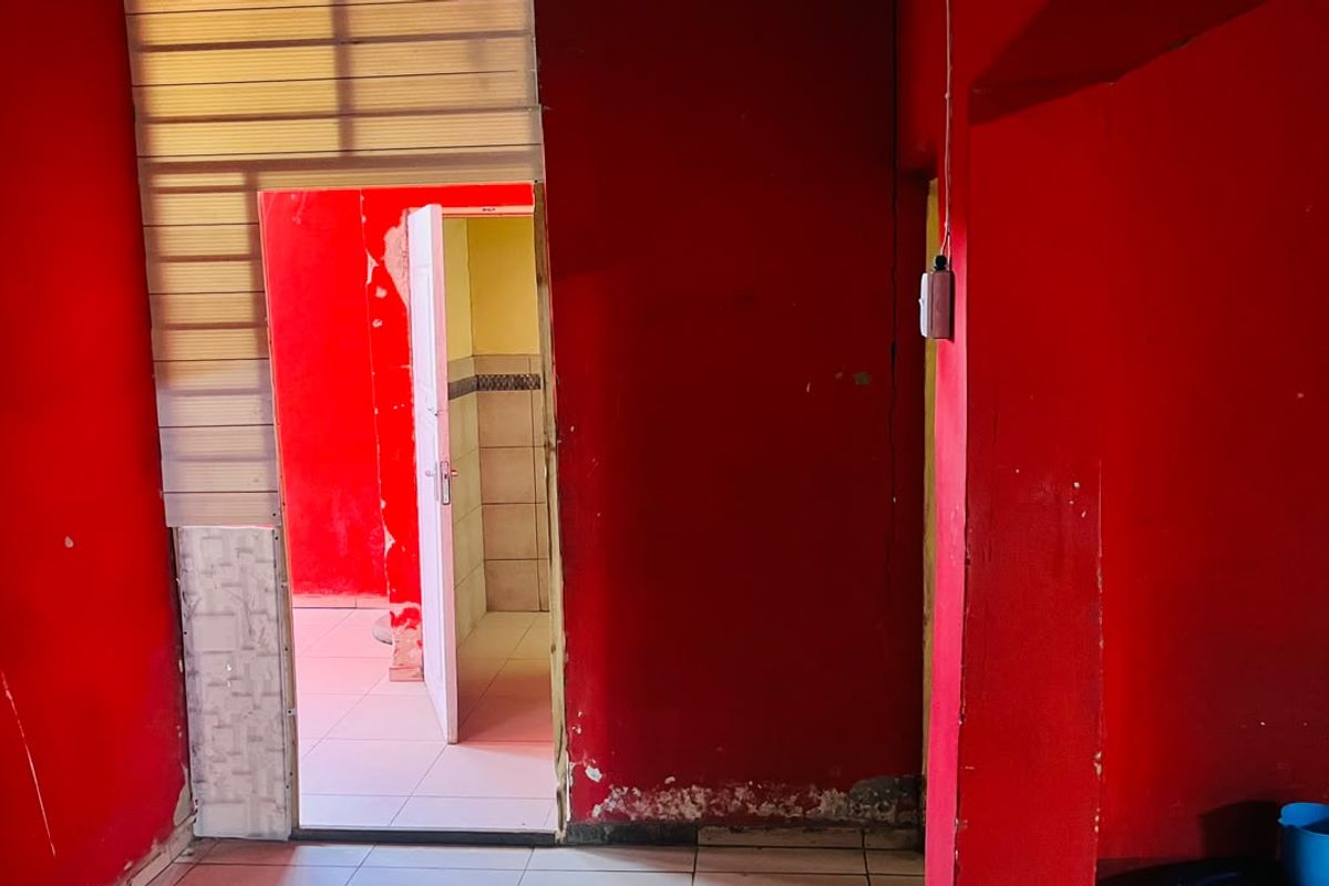 An empty interior space featuring tiled flooring and bright red walls, showing significant signs of wear and requiring cosmetic refurbishment.