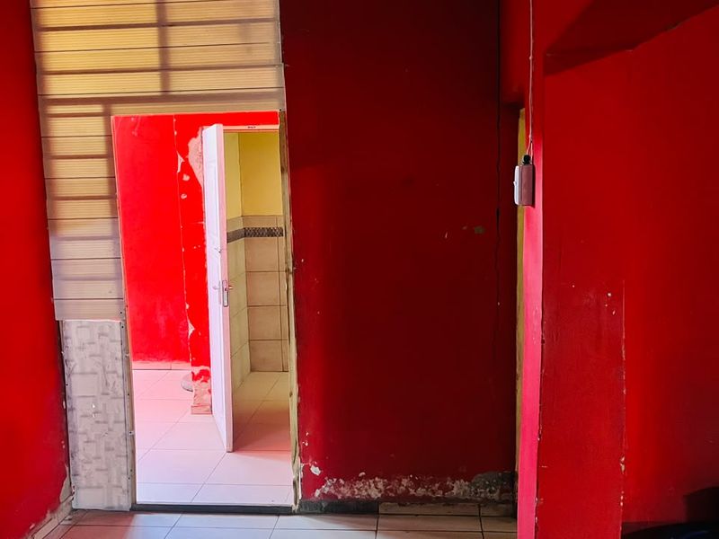 An empty interior space featuring tiled flooring and bright red walls, showing significant signs of wear and requiring cosmetic refurbishment.