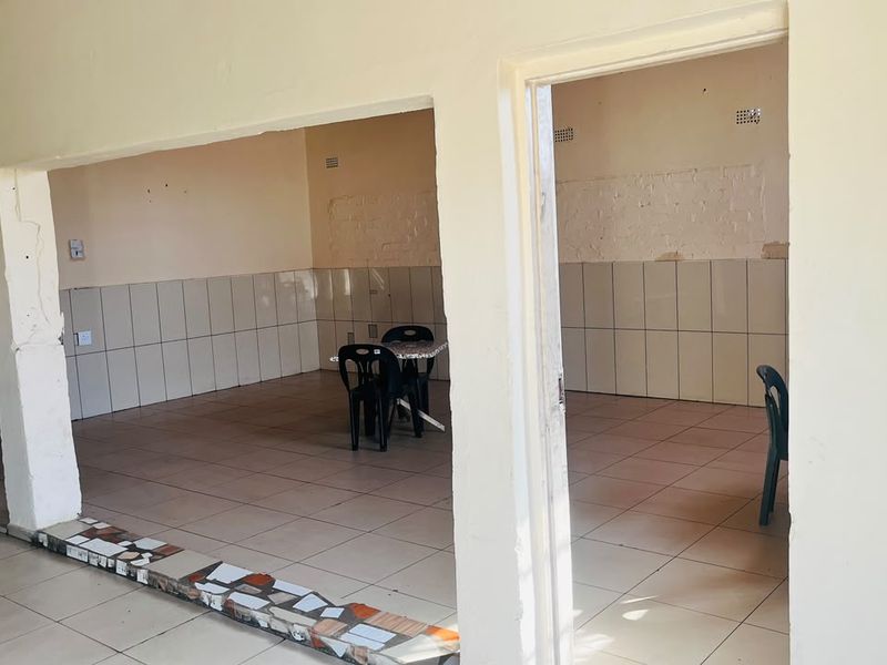 An open-plan commercial space featuring tiled flooring and partial wall tiling, requiring cosmetic updates and repairs to wall finishes.