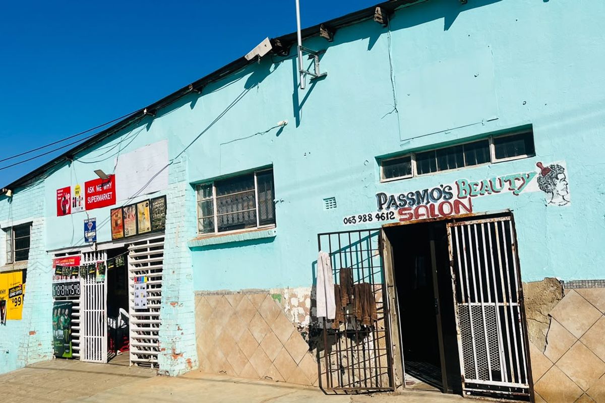 Front facade of a commercial building featuring painted brickwork, security gates, and tiled base detailing, showing signs of significant wear and maintenance requirements.