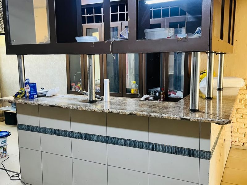 A functional bar area featuring a granite countertop, tiled base, and overhead cabinetry, suitable for hospitality or commercial use.