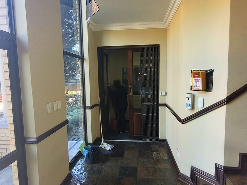 A bright office entrance foyer featuring slate tile flooring, decorative crown molding, and a secure wooden door with an integrated security gate.