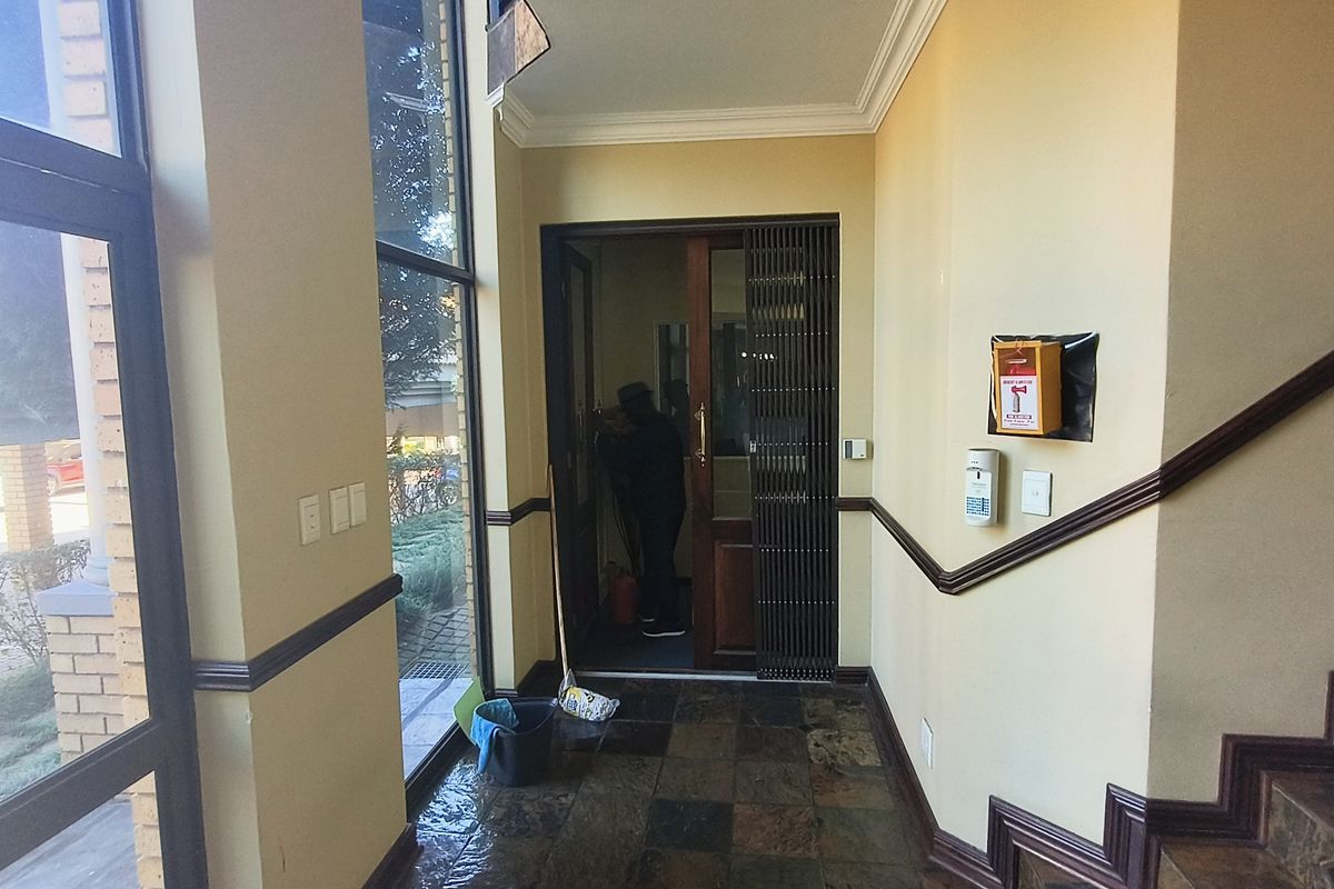 A bright office entrance foyer featuring slate tile flooring, decorative crown molding, and a secure wooden door with an integrated security gate.
