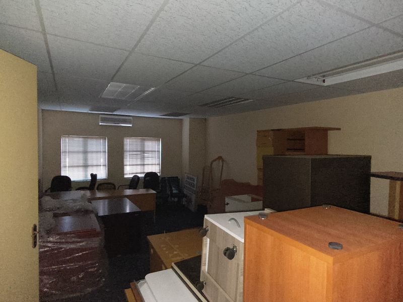 A functional office space featuring a suspended ceiling, recessed lighting, and a wall-mounted air conditioning unit, currently used for storage.