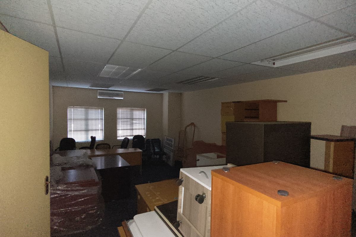 A functional office space featuring a suspended ceiling, recessed lighting, and a wall-mounted air conditioning unit, currently used for storage.