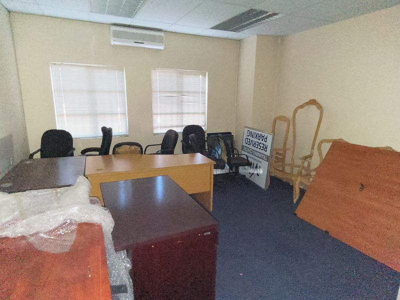 A functional office space featuring a suspended ceiling, split-system air conditioning, and dual windows with venetian blinds, currently used for storage.