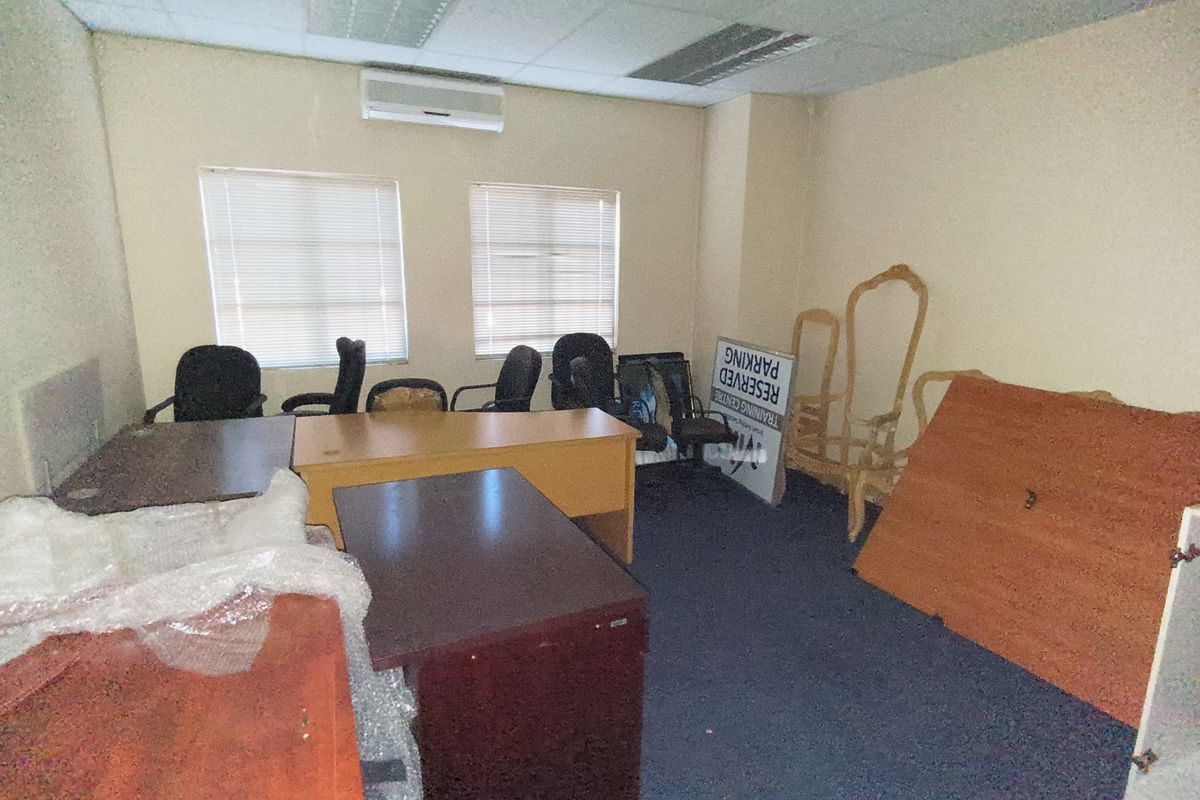 A functional office space featuring a suspended ceiling, split-system air conditioning, and dual windows with venetian blinds, currently used for storage.