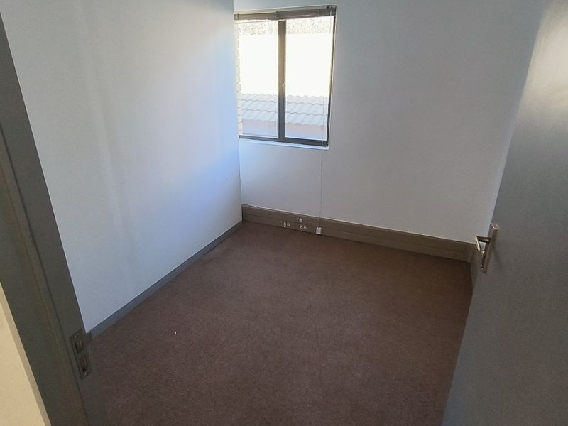 A compact, empty office space featuring neutral walls, carpeted flooring, and a window providing natural light.