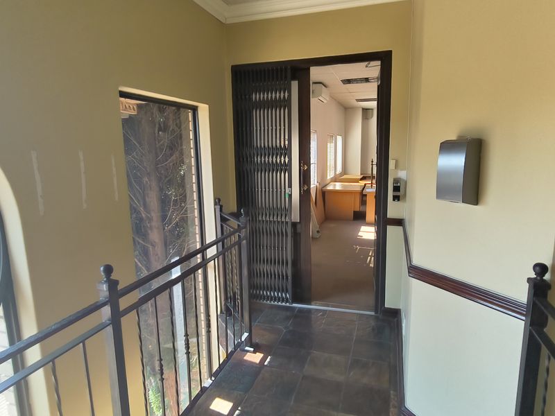 A well-lit hallway featuring tiled flooring, a decorative circular window, wrought iron balustrades, and a secure metal gate leading into an office space.