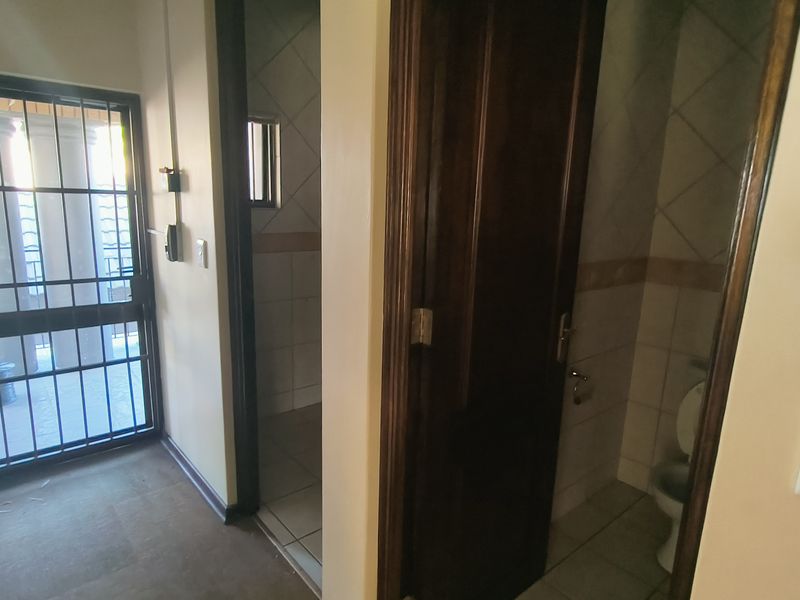 A functional office hallway featuring a security gate, tiled flooring, and access to adjacent rooms with wooden doors.