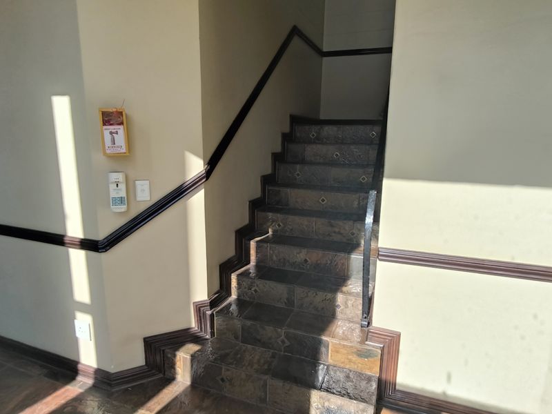 A functional office hallway featuring a tiled staircase with a handrail, wall-mounted intercom, and fire safety equipment.