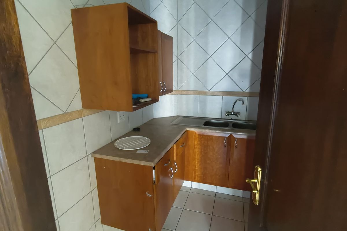 A compact kitchenette featuring wooden cabinetry, a stainless steel sink, and tiled finishes, offering a functional space for office staff.