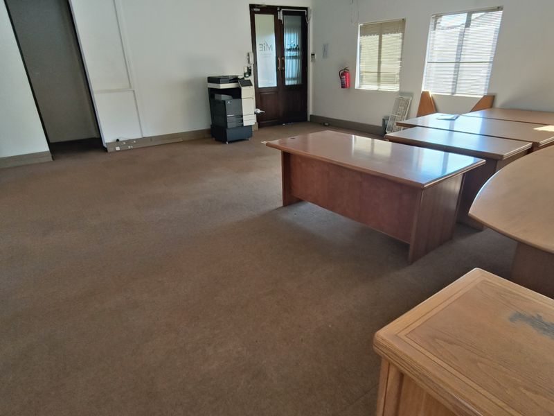 A functional office space featuring carpeted flooring, venetian blinds, and a fire extinguisher, providing a practical layout for professional use.