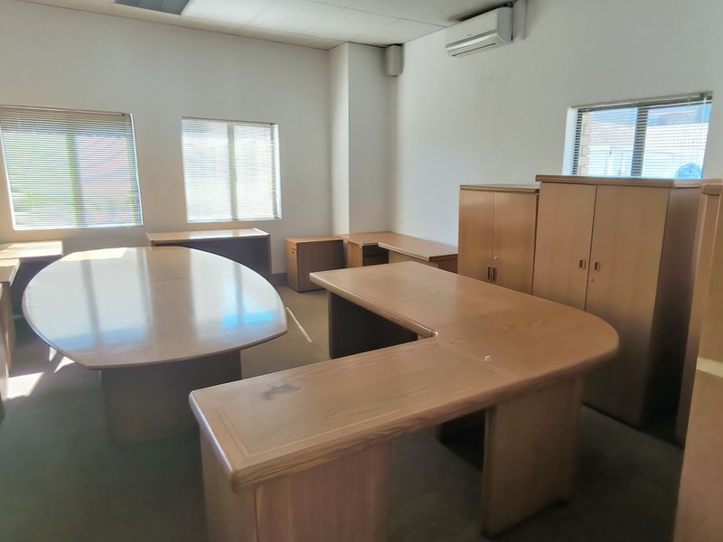 A functional office space featuring built-in wooden cabinetry, air conditioning, and large windows with venetian blinds, providing a practical workspace environment.