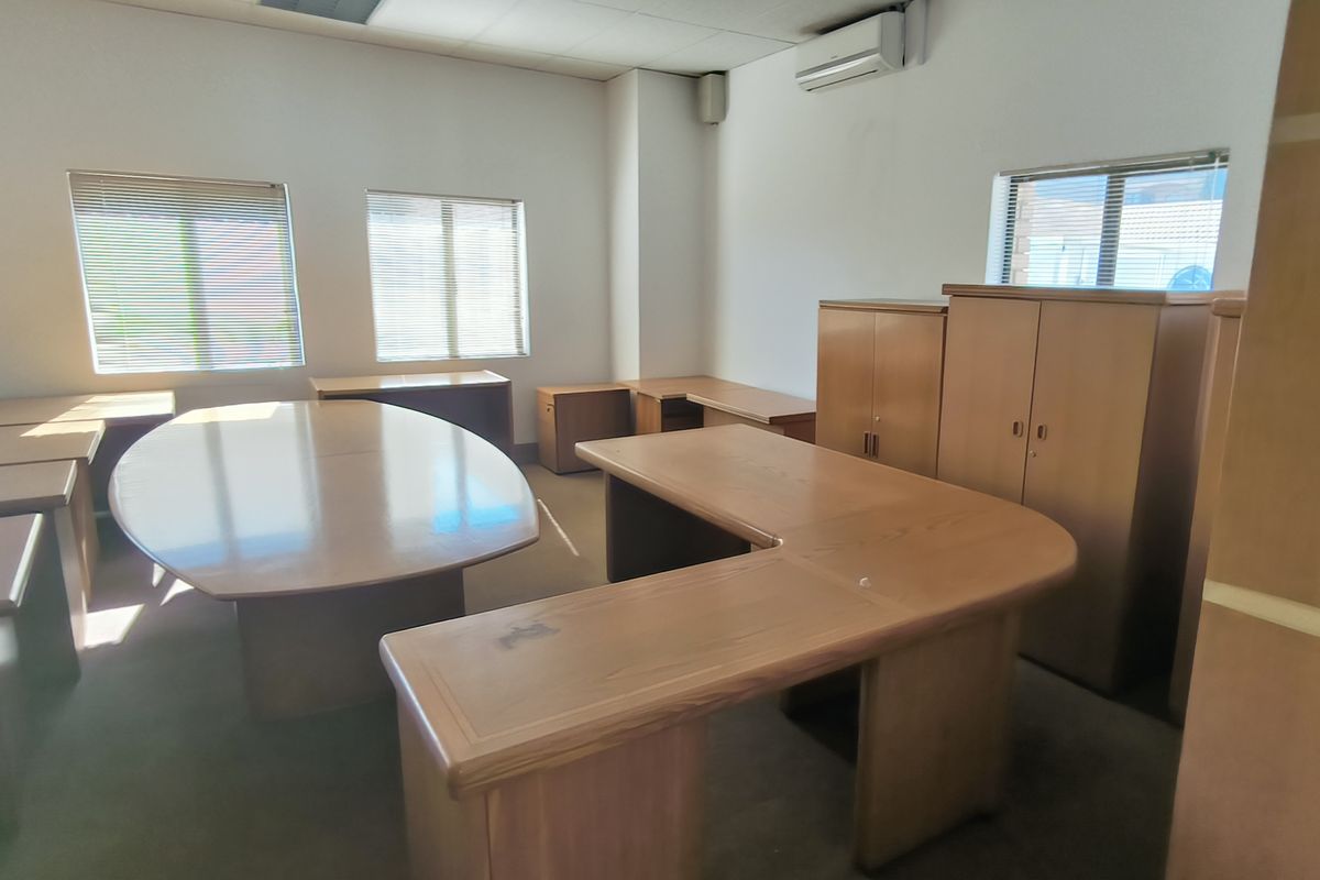 A functional office space featuring built-in wooden cabinetry, air conditioning, and large windows with venetian blinds, providing a practical workspace environment.