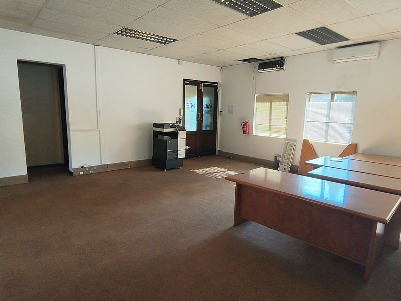 Spacious office area featuring suspended ceilings, air conditioning, and large windows with blinds, offering a functional workspace in need of cosmetic updates.