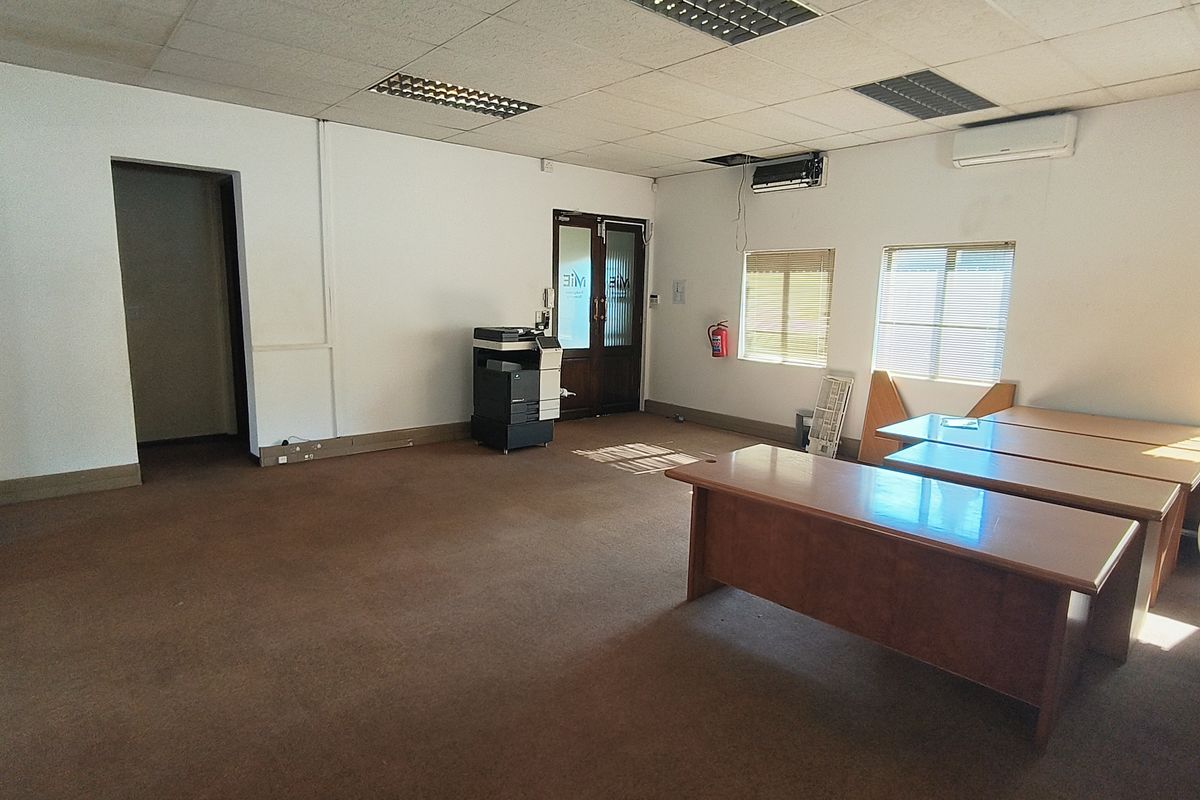 Spacious office area featuring suspended ceilings, air conditioning, and large windows with blinds, offering a functional workspace in need of cosmetic updates.
