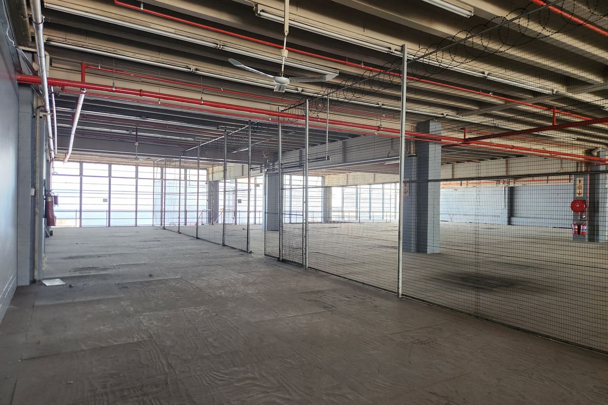 Expansive industrial utility space featuring exposed fire sprinkler systems, wire mesh partitioning, and large windows providing ample natural light.