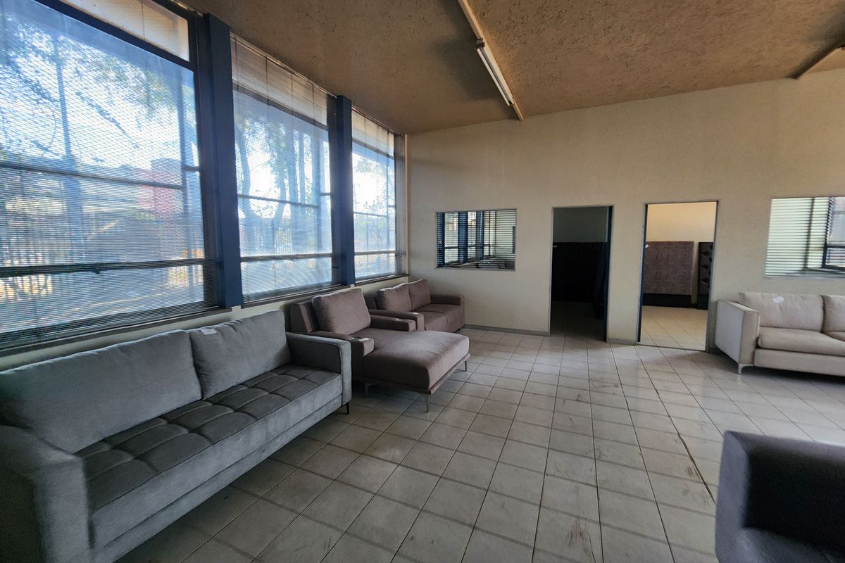 Spacious industrial-style room featuring large windows, tiled flooring, and multiple internal access points, suitable for a showroom or office waiting area.