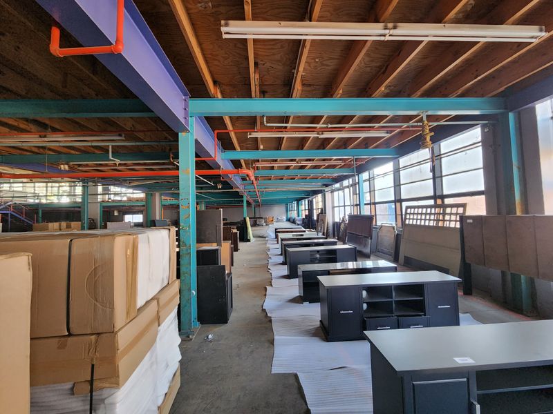 Spacious industrial warehouse area featuring exposed timber joists, painted steel structural beams, fire sprinkler system, and large windows providing ample natural light.