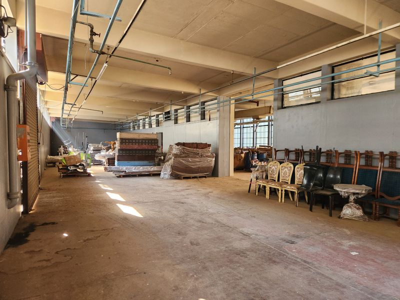 Spacious industrial utility area featuring exposed ceiling beams, high-level windows, and durable concrete flooring, suitable for storage or workshop use.