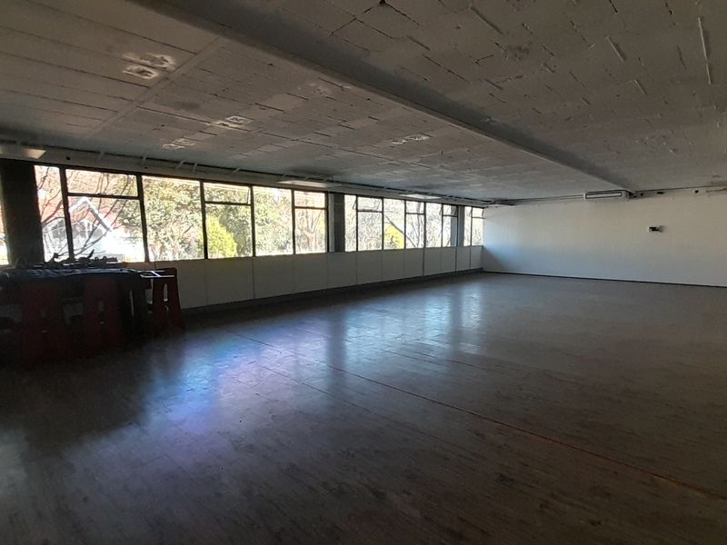 Spacious open-plan office area featuring large windows, exposed concrete ceilings, and laminate flooring, offering a versatile workspace with abundant natural light.