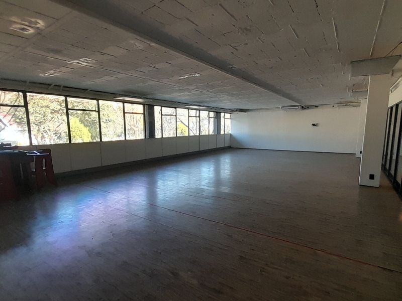 Spacious open-plan office area featuring large windows, exposed concrete ceilings, and glass partitioning, offering a versatile workspace with natural light.